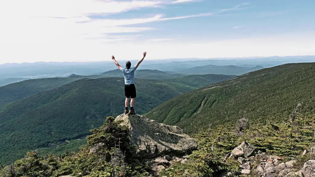 A person joyfully stretching and celebrating at the summit of a mountain.