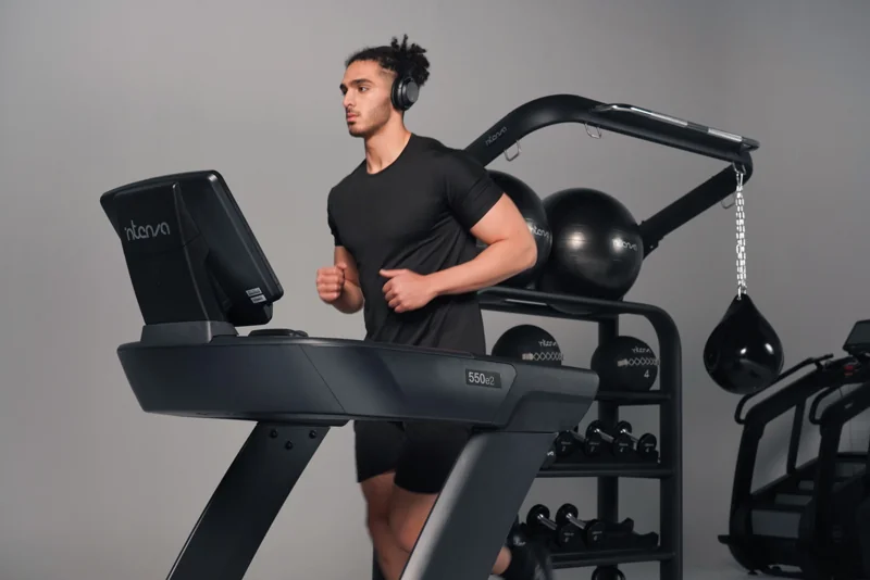 Man running on Intenza 550 e2 treadmill in modern gym with functional training equipment in background