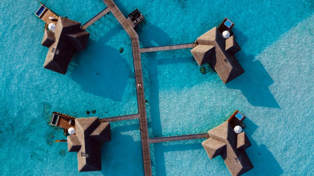 Overwater villas connected by wooden walkways above turquoise water at a luxury resort