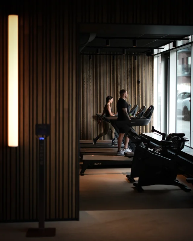 Man and woman using Intenza treadmills in boutique gym with wood panel walls and natural light